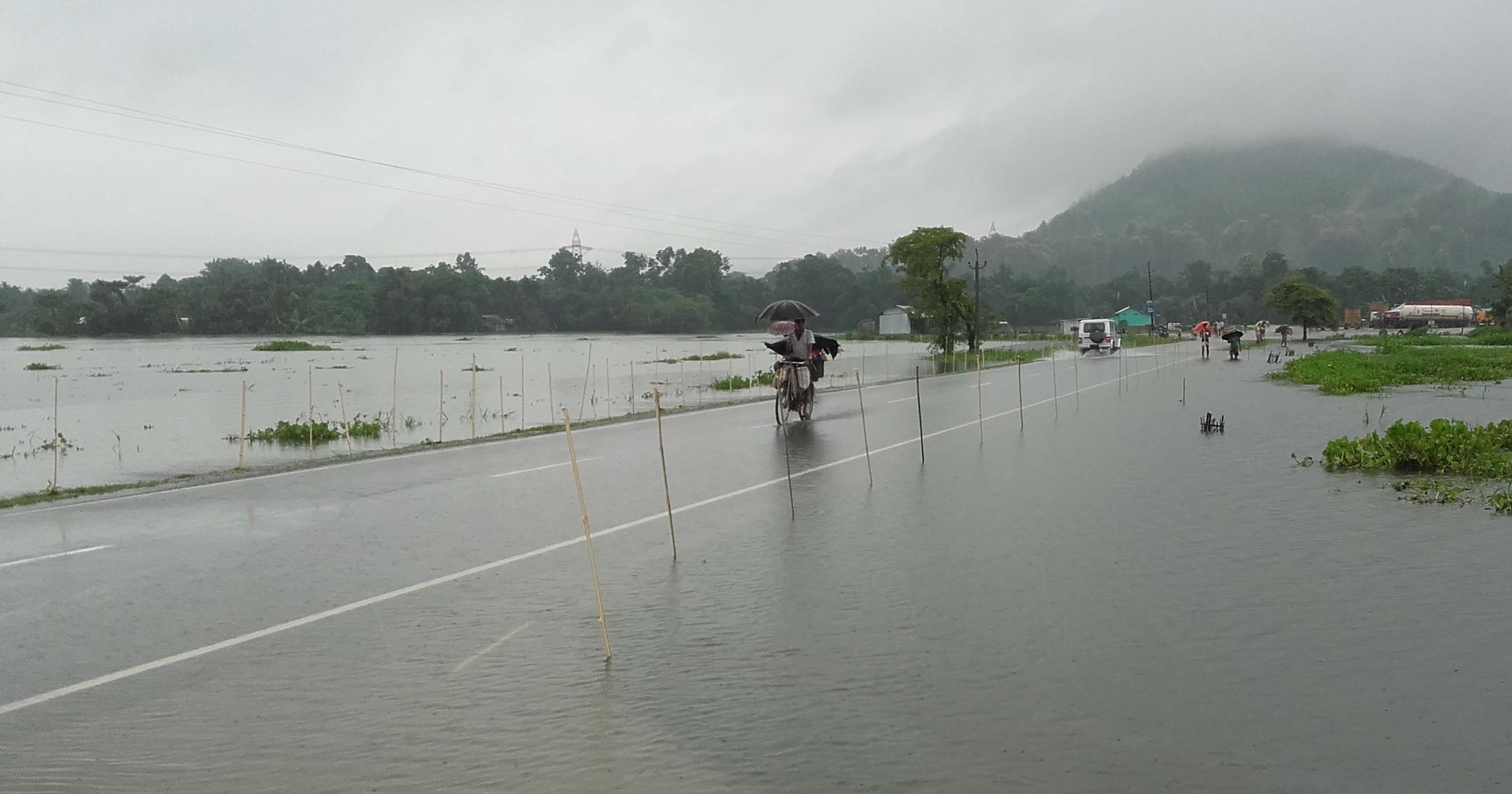 People passing in flooded NH 31 at Jharaguri jn Bongaigaon on Saturday. Photo by UB Photos.